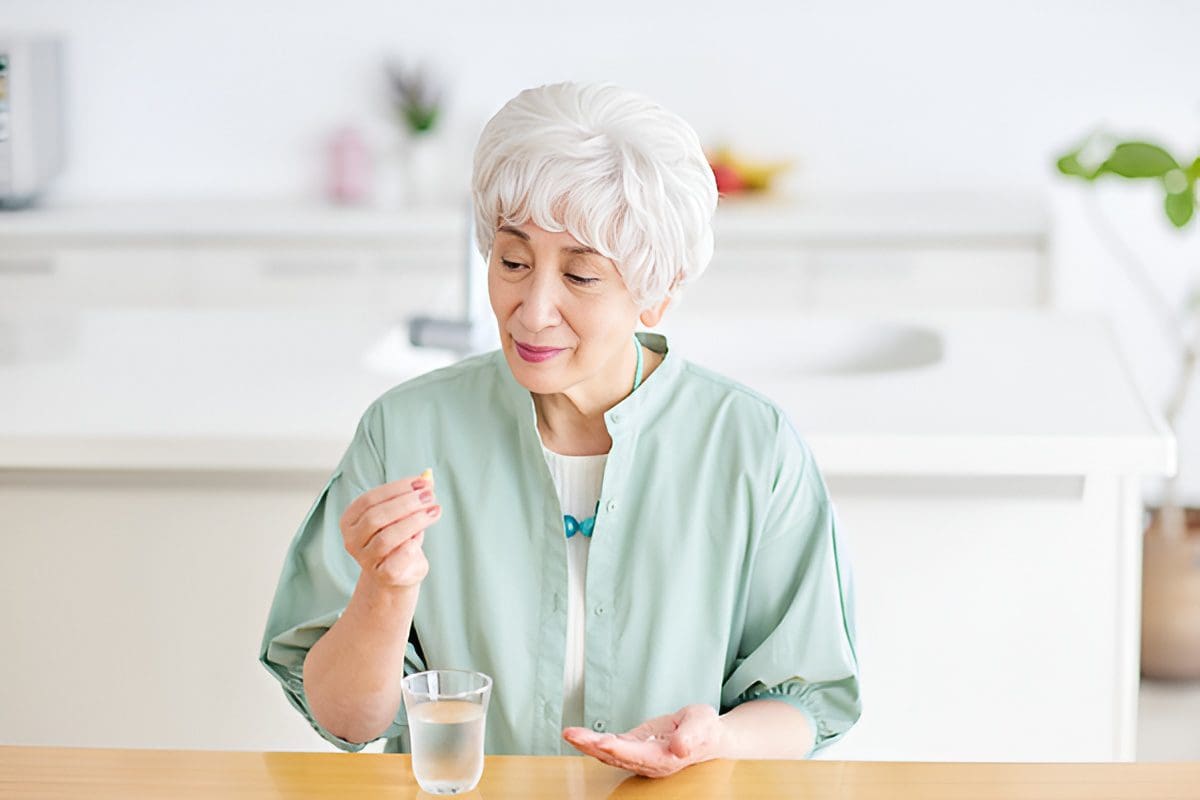Elderly woman taking medication with a glass of water.